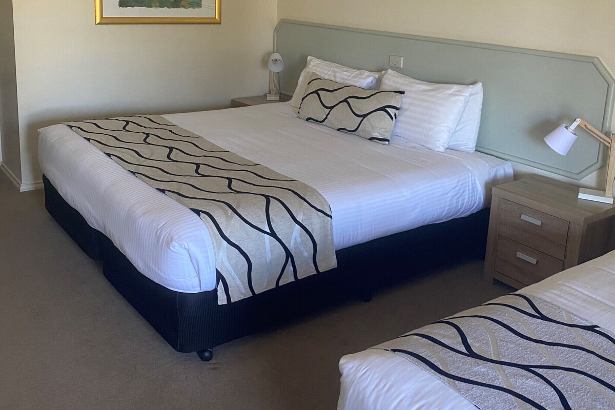 A hotel room with a large bed, a smaller bed, a nightstand with a lamp, and a framed picture on the wall.