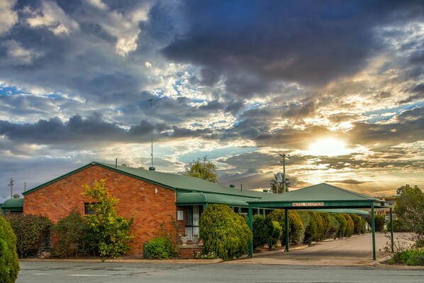 A motel reception with a brick building and a green roof, surrounded by greenery.
