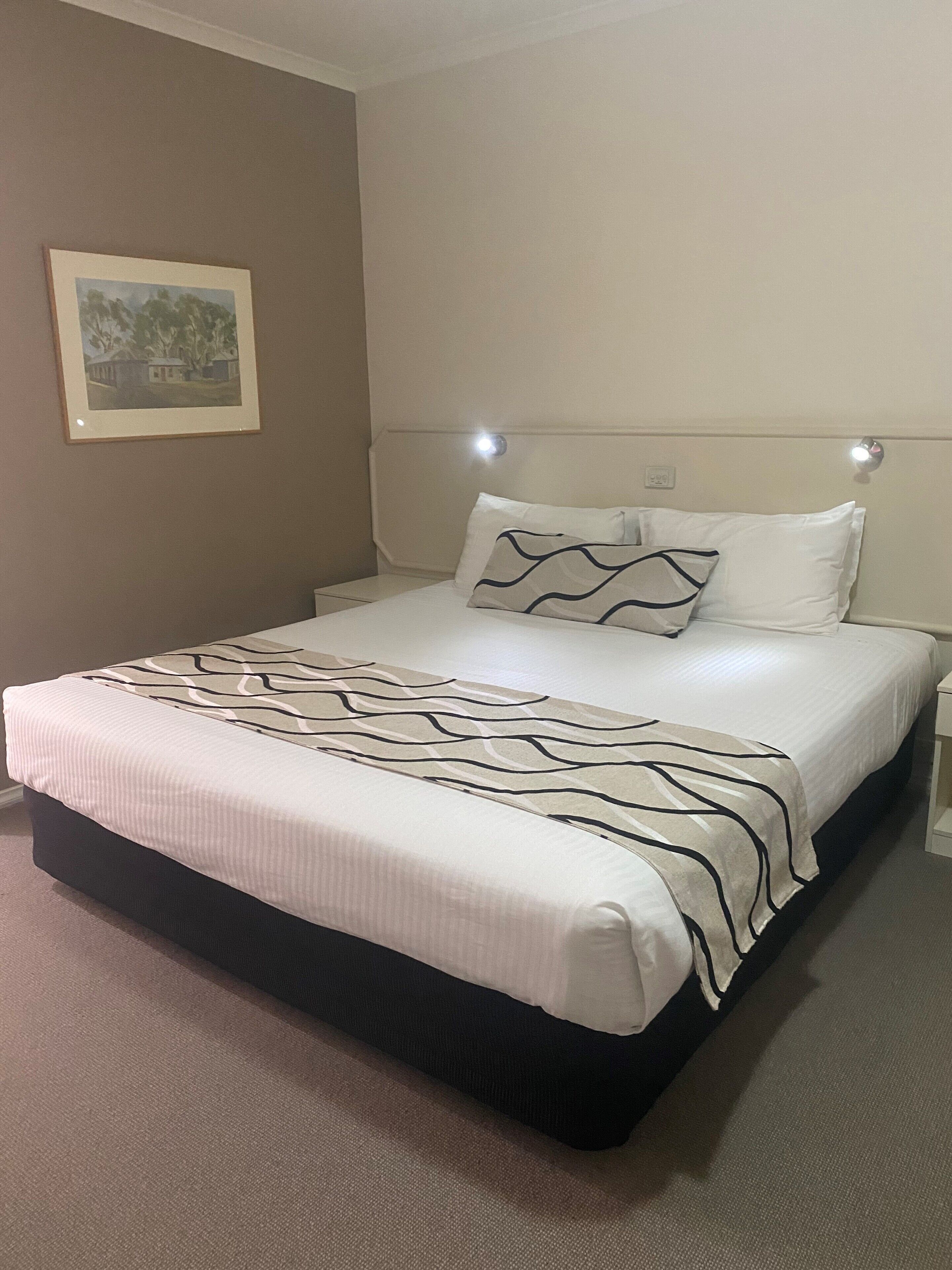 A neatly made bed with a patterned bedspread, a headboard with integrated lighting, and a framed picture on the wall.