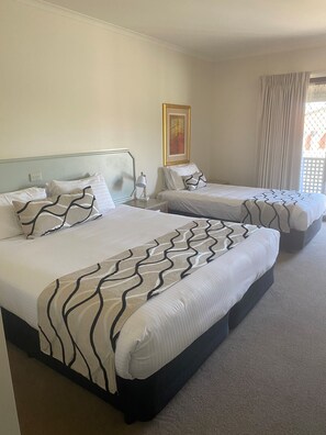 A hotel room with two beds, each with a patterned bedspread, a bedside table with a lamp, and a painting on the wall. - Deniliquin Country Club Motor Inn (Deniliquin)