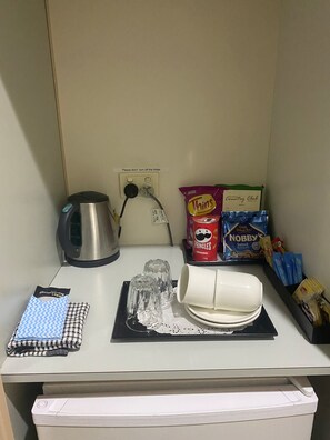 A kitchenette with a kettle, a coffee maker, a tea kettle, a microwave, a coffee cup, a glass, a tea bag, a packet of pringles, a packet of nobby's peanuts, and a packet of thins. - Deniliquin Country Club Motor Inn (Deniliquin)