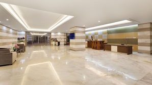 Un hall d’hôtel moderne comprenant un comptoir d’accueil, un espace salon et un ascenseur en verre.