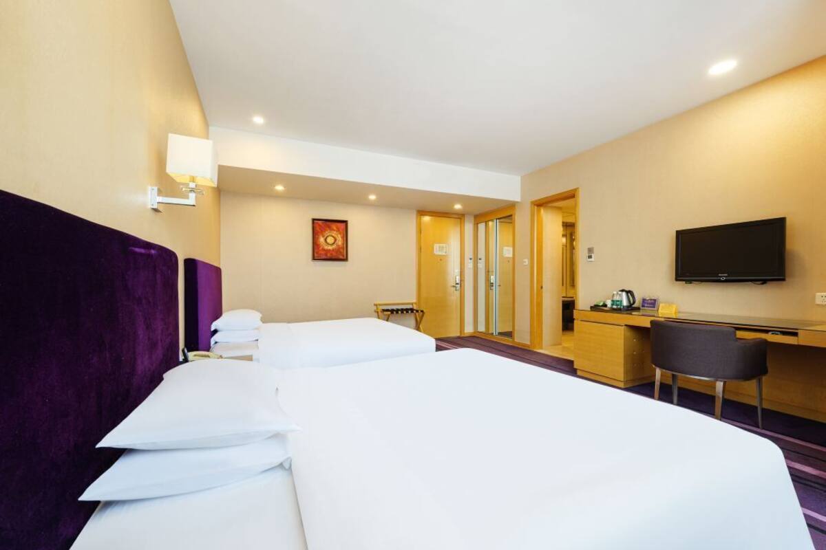 Habitación de hotel con dos camas, un escritorio, una silla, un televisor y un baño visible a través de una puerta abierta.