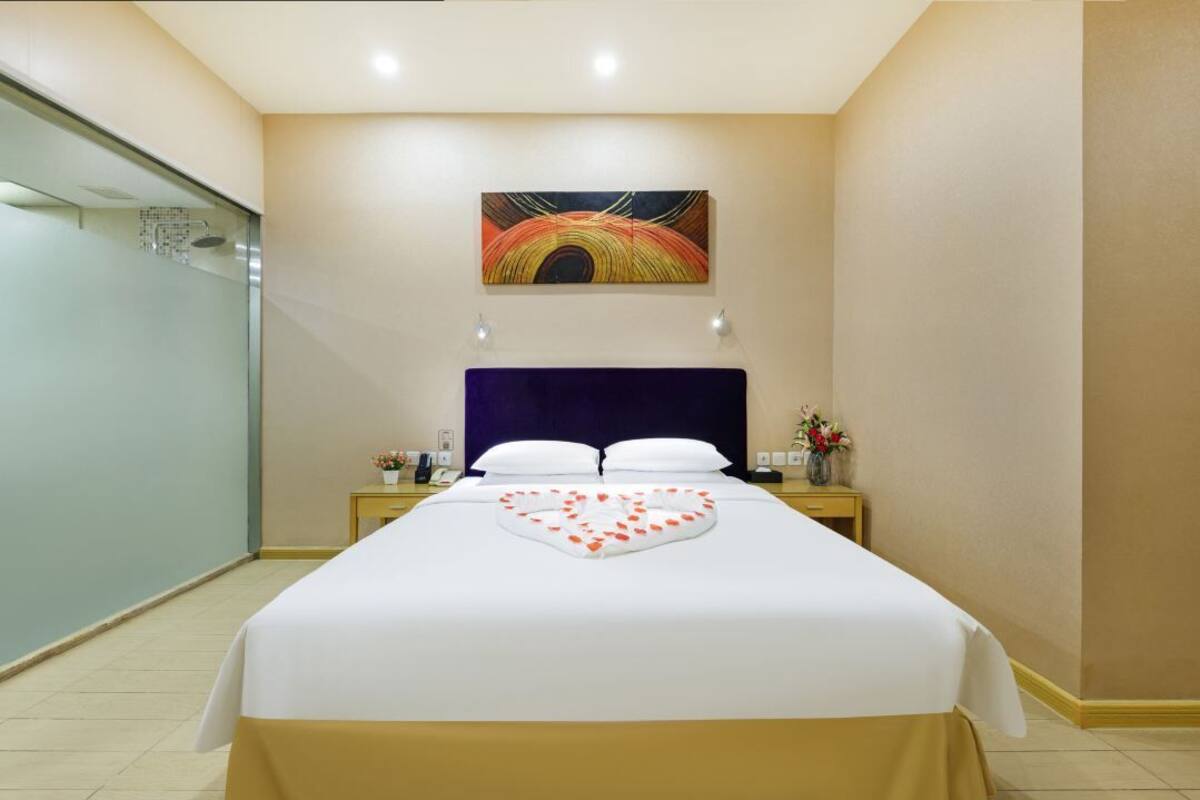 Una habitación de hotel con una cama, un cuadro en la pared y una mesita de noche con un florero.