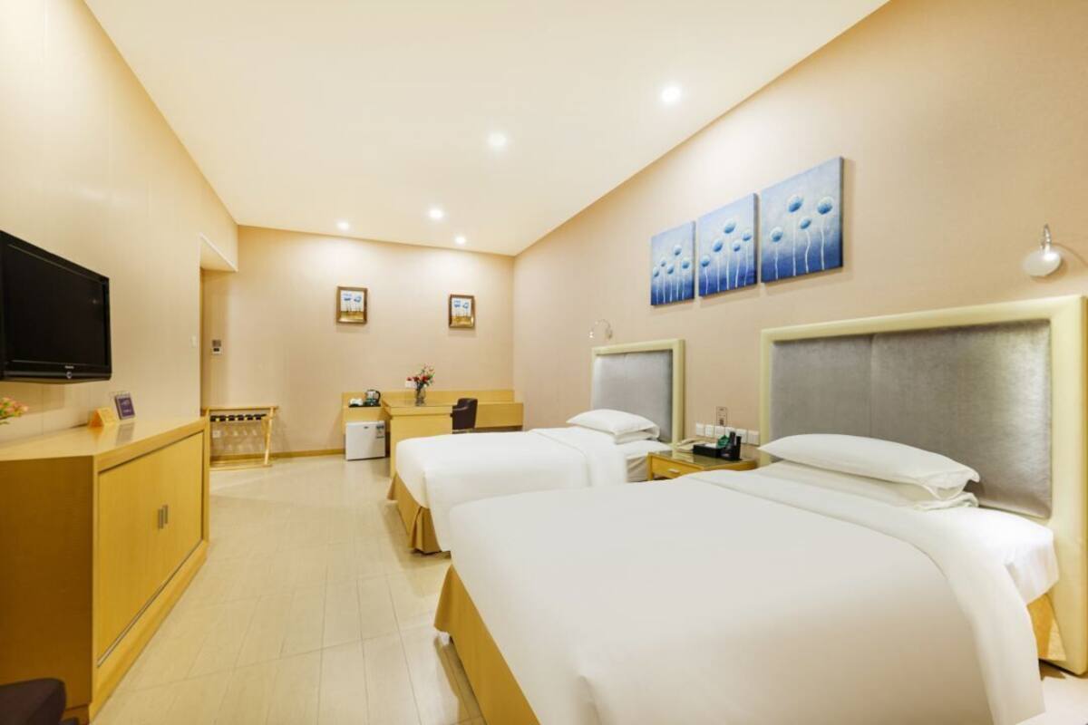 Una habitación de hotel con tres camas, un escritorio, un televisor y obras de arte en la pared.