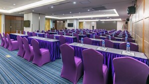 Une salle de conférence avec des rangées de tables et des chaises violettes, équipée de bouteilles d’eau et de blocs-notes.