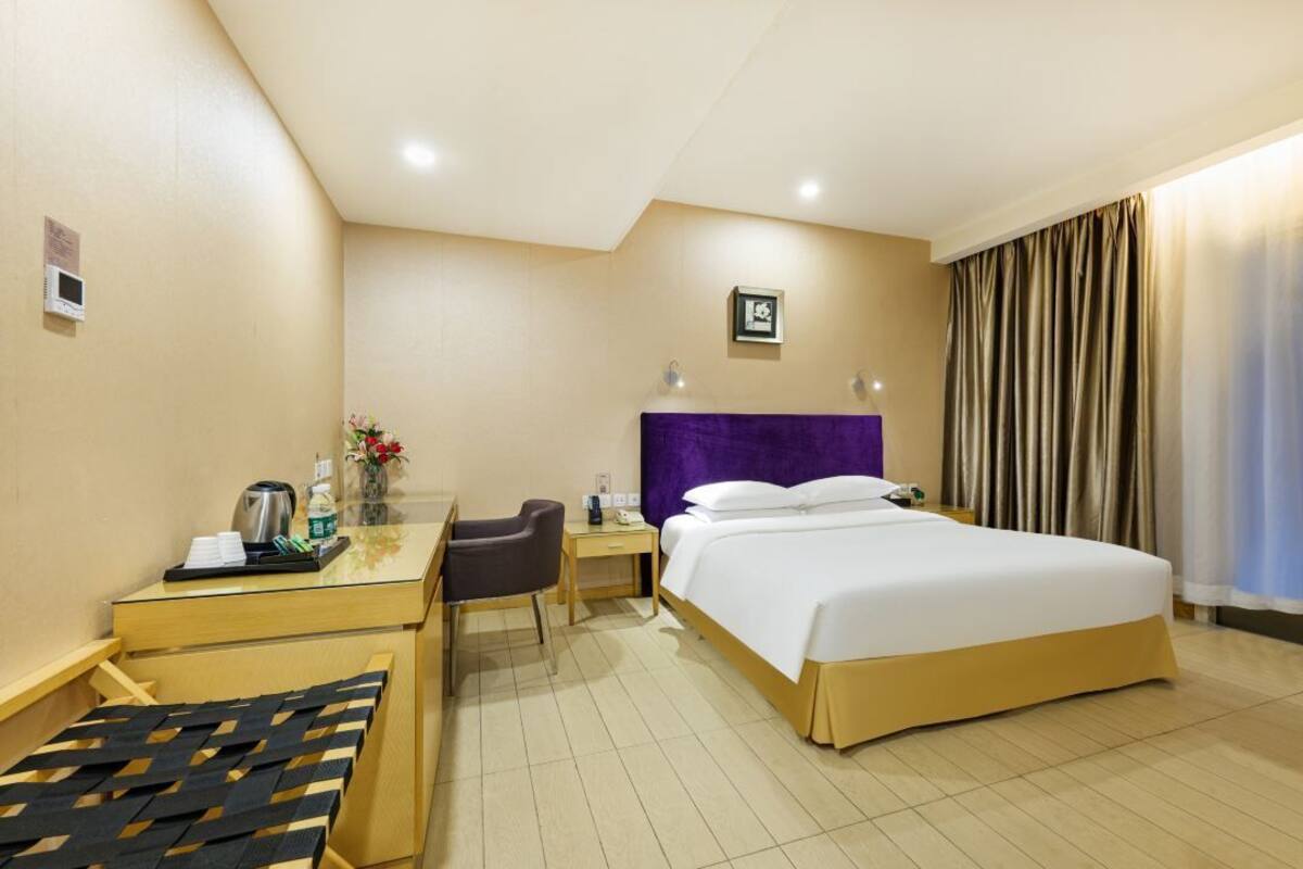 Una habitación de hotel con una cama, un escritorio con silla, una mesita pequeña y una ventana con cortinas.