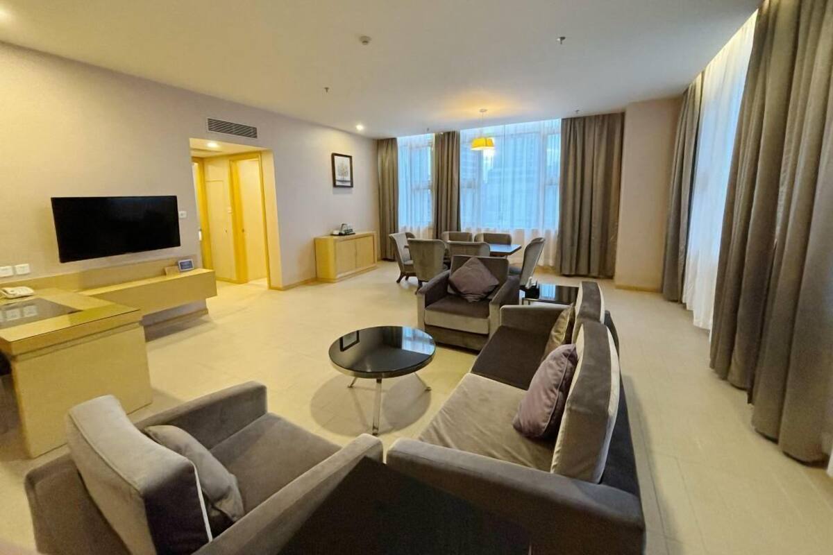 Una habitación de hotel moderna con sala de estar, televisor de pantalla plana, juegos de sofá, mesa de comedor y una pequeña cocina.