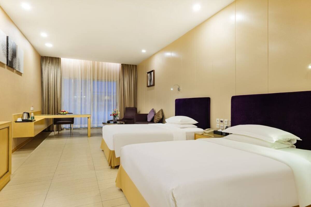 Una habitación de hotel con dos camas, un escritorio, una silla y un ventanal con cortinas.