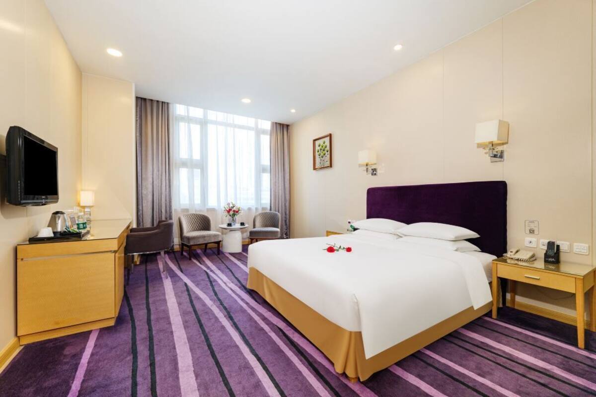 Habitación de hotel con una cama grande, un escritorio, un televisor y una zona de estar con sillas y una mesa.