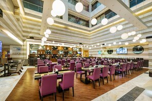 A spacious dining area with purple chairs and tables, a bar area with a TV, and a high ceiling with hanging lights. - The Bauhinia Hotel Shenzhen  (Shenzhen)
