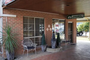 Un edificio de ladrillo con una zona de recepción, dos sillas de metal blanco y plantas en macetas.