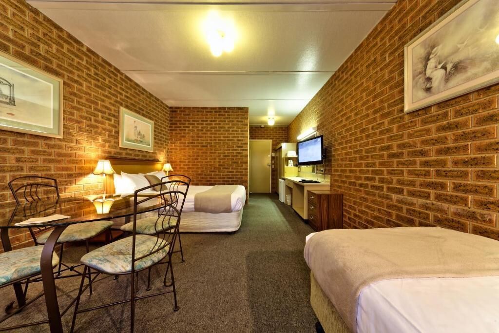 Habitación de hotel con paredes de ladrillo, una cama, un escritorio con computadora, una silla y una mesita con lámpara.