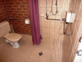Un baño con inodoro, ducha con barras de apoyo y cortina de ducha morada.