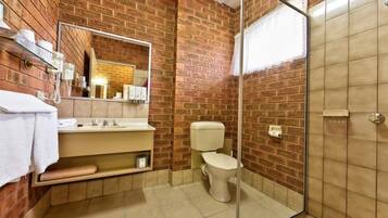 Baño con pared de ladrillo, cabina de ducha de vidrio, inodoro y lavamanos con espejo superior.