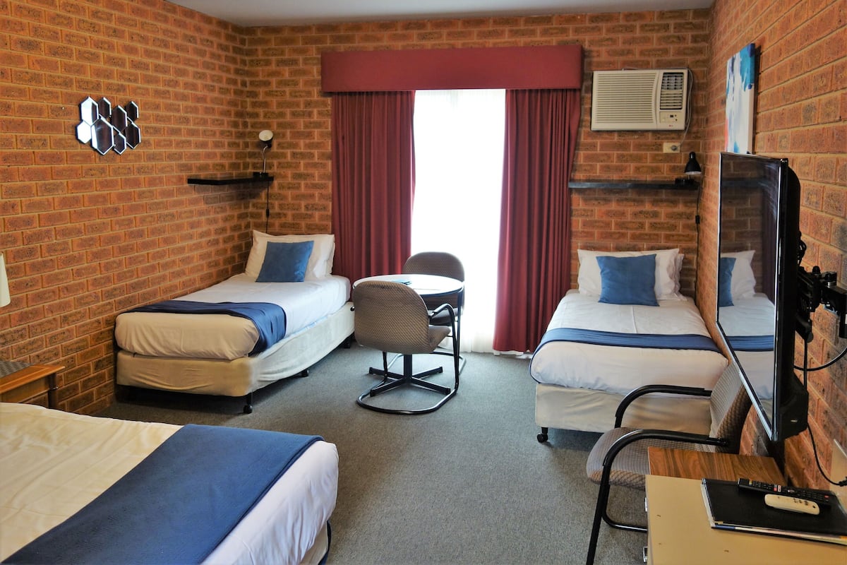 Habitación de hotel con dos camas individuales, un escritorio, una silla, un televisor y una pared de ladrillo.