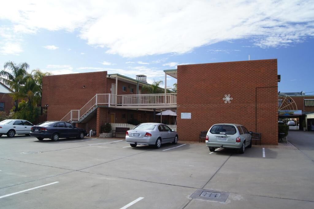 A parking lot with several cars, a building with a brick facade, and a staircase leading to a balcony.