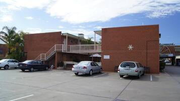 A parking lot with several cars, a building with a brick facade, and a staircase leading to a balcony.
