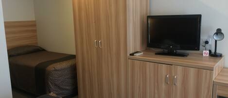 A hotel room with a bed, a TV, a desk with a computer, and a wardrobe.