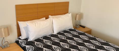 A neatly made bed with a patterned bedspread, two bedside tables with lamps, a framed picture on the wall, and a small wooden nightstand.