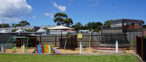 A fenced backyard with a playground, including swings and slides, and a wooden fence.