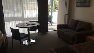 Habitación de hotel con sofá, una mesa de comedor con dos sillas, una pequeña cocina y un ventanal con cortinas.