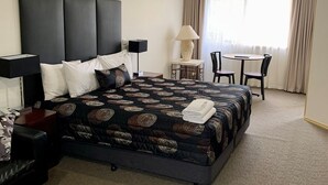 Een hotelkamer met een groot bed, een bureau met stoel, een lamp en uitzicht op het landschap door een raam.