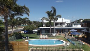Un espace piscine avec des chaises longues, une clôture et un bâtiment en arrière-plan.