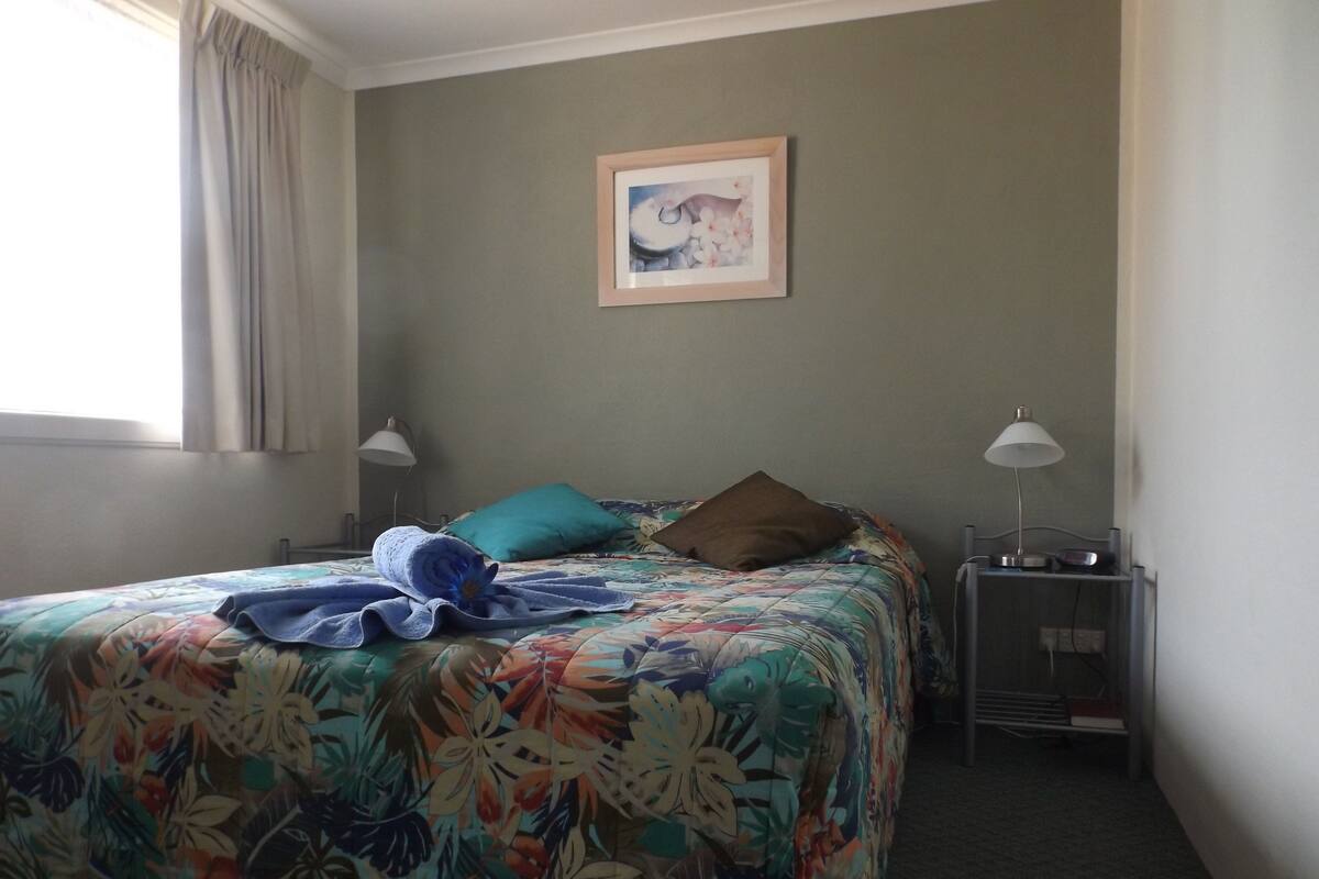 Habitación de hotel con colcha estampada, un cuadro enmarcado en la pared y dos lámparas de noche.