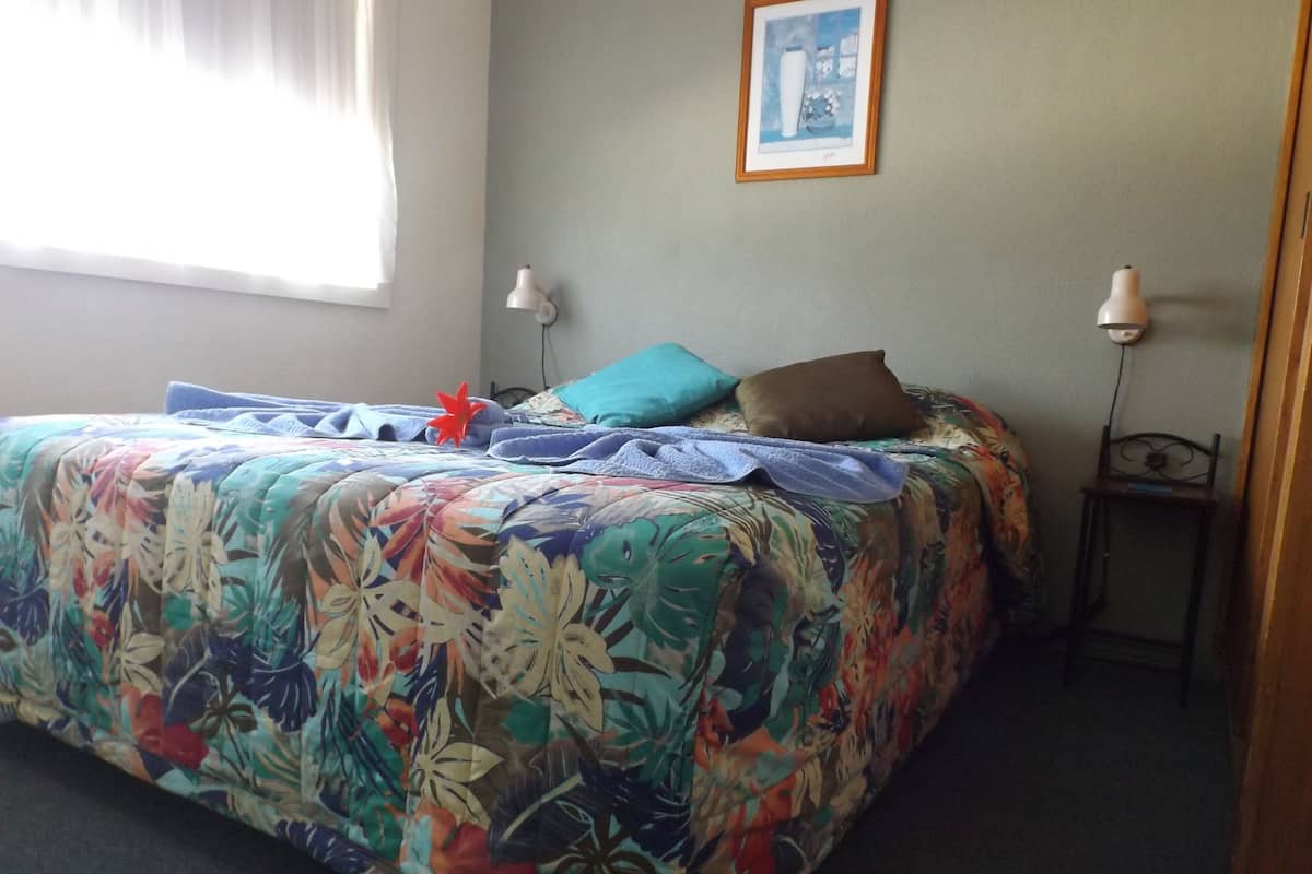 Una cama con una colcha estampada, dos lámparas de noche y un cuadro en la pared.