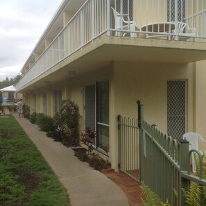 A row of single-story buildings with balconies, a paved walkway, and a green fence. - Bayshores Holiday Apartments (Torquay)