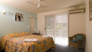 Une chambre à coucher avec un lit, une chaise, un ventilateur de plafond et une fenêtre avec des stores.