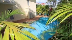 Une piscine entourée d’une végétation luxuriante et un bâtiment doté d’un balcon.