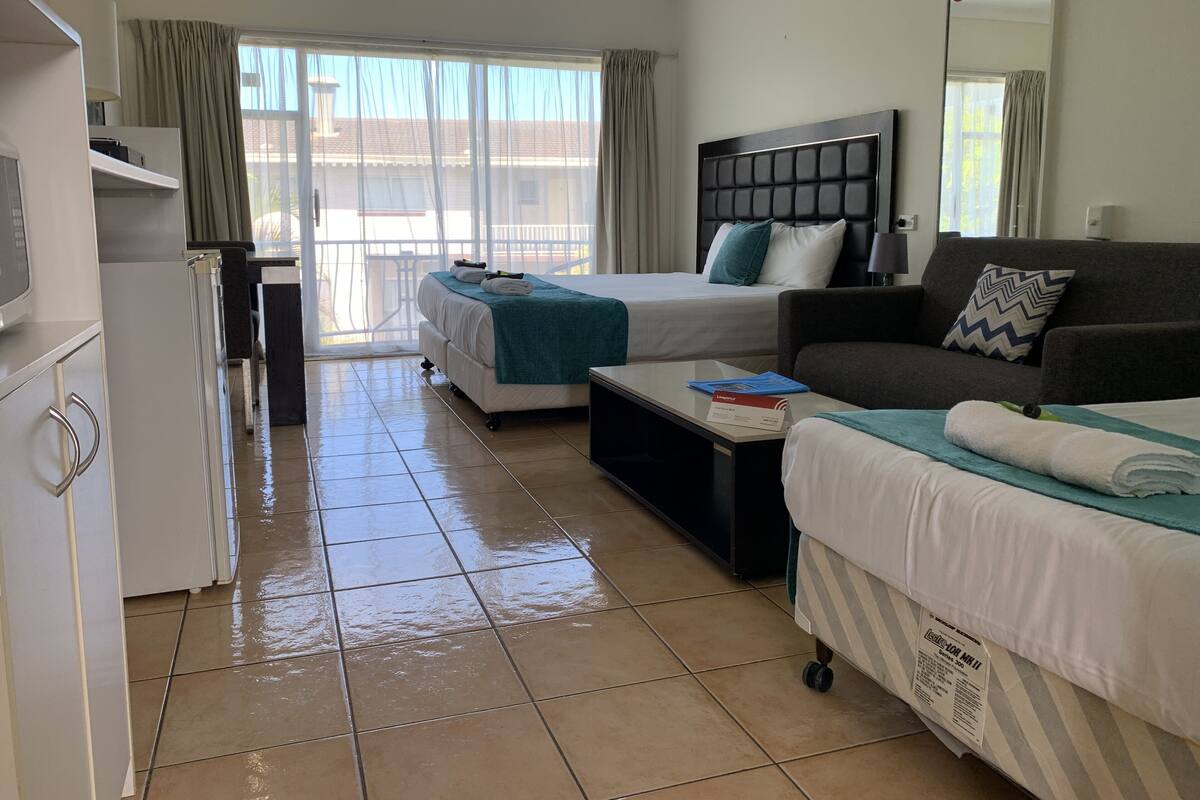 A hotel room with two beds, a sofa, a desk, and a kitchenette.