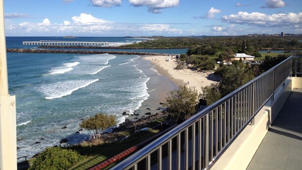 A coastal view with a beach, ocean waves, a pier, and a building in the background. - Tweed Central Motel (Tweed Heads)