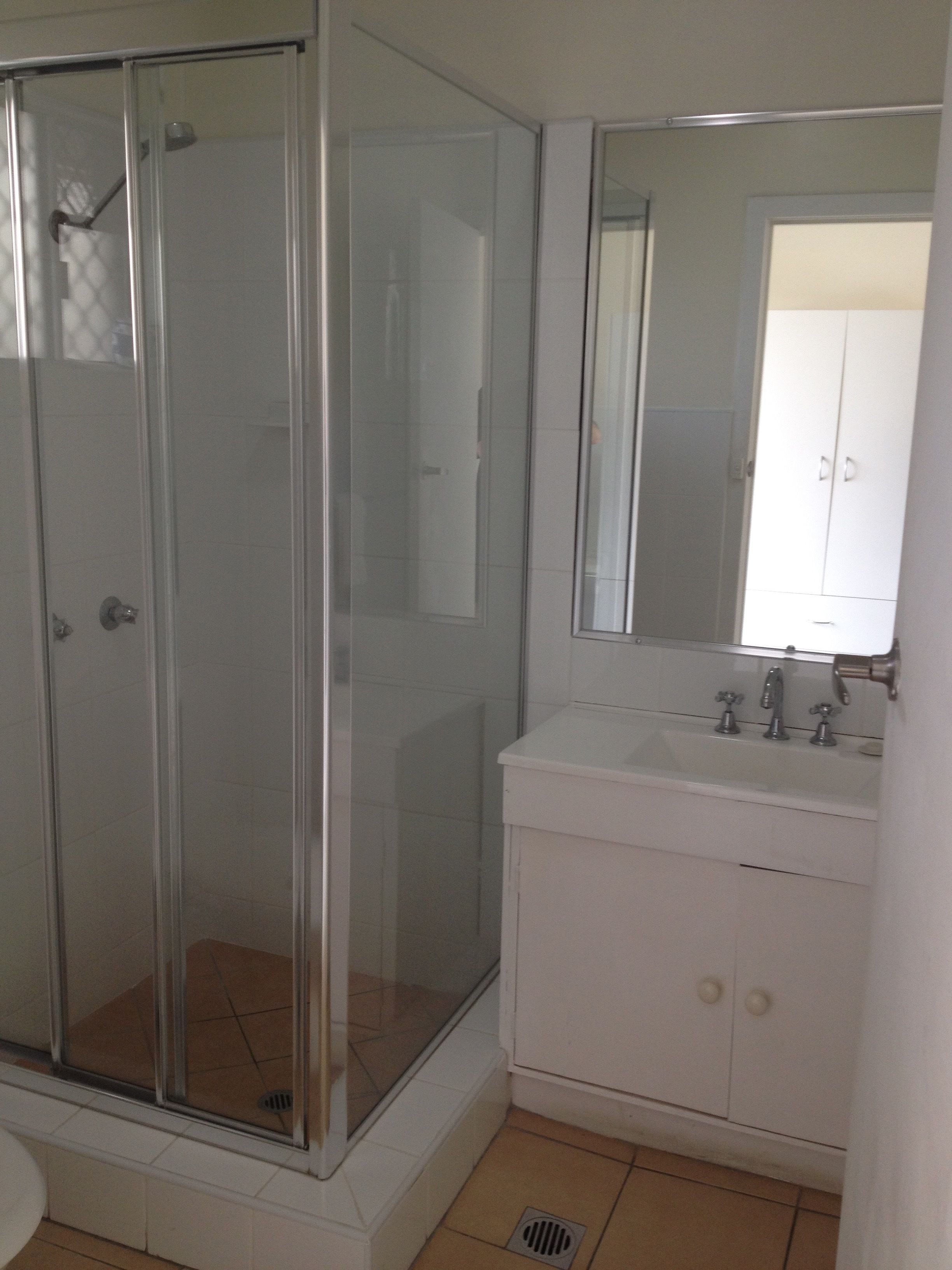 A bathroom with a glass-enclosed shower, a white sink with two faucets, and a cabinet with two drawers.