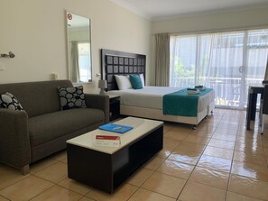 A hotel room with a sofa, a bed with a headboard, a coffee table, and a large window with curtains. - Tweed Central Motel (Tweed Heads)