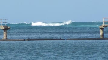 A pier with concrete pillars and a railing, extending into a body of water with waves.
