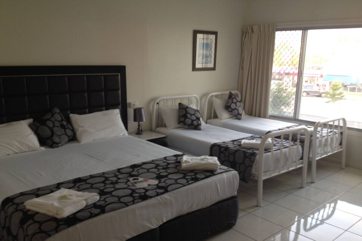 A hotel room with two beds, a window with curtains, and a view of the outside.