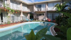 A swimming pool surrounded by a fence, with a building in the background. - Tweed Central Motel (Tweed Heads)