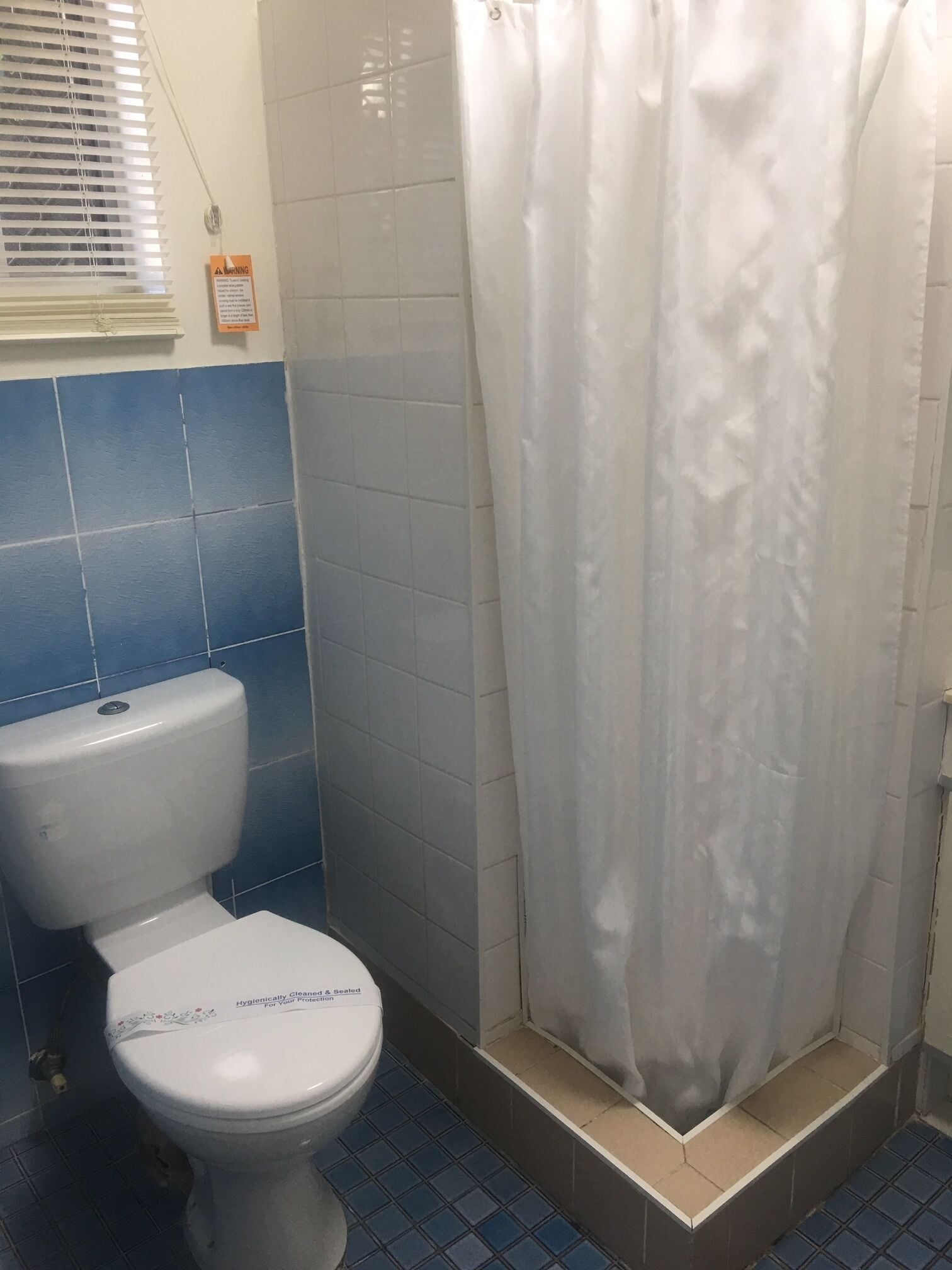 A bathroom with a toilet, a shower curtain, and blue and white tiled walls.