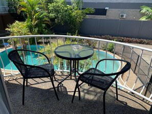 A balcony with a glass table and two chairs, overlooking a swimming pool surrounded by greenery. - Tweed Central Motel (Tweed Heads)