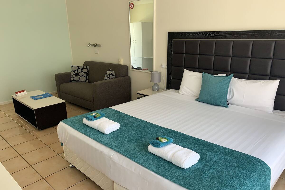 A hotel room with a large bed, a sofa, a small table, and a mirror.