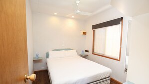 Ein Hotelzimmer mit Bett, Nachttisch, Fenster und Deckenventilator.