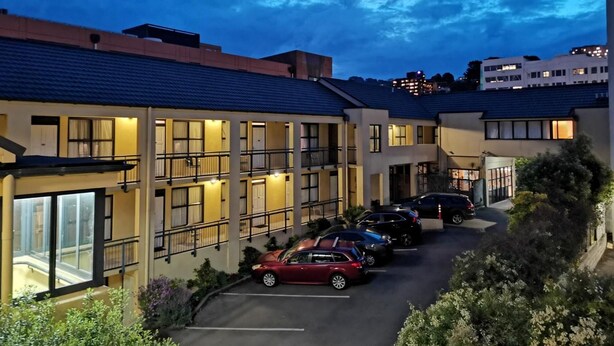 A multi-story hotel with a parking lot and a view of the city skyline at dusk. - Victoria Court Motor Lodge (Wellington)