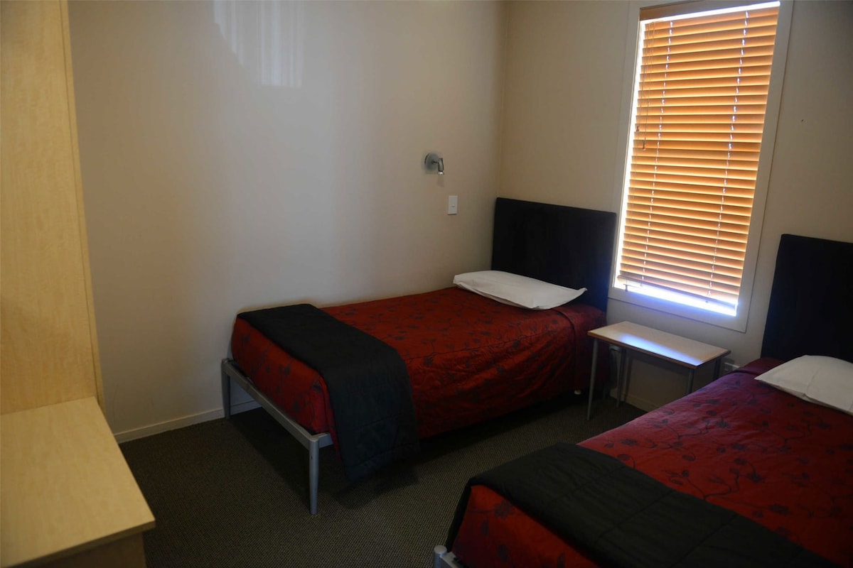 A room with two single beds, a small table, and a window with blinds.