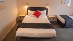 A hotel room with a large bed, two bedside tables, and a small table. - Victoria Court Motor Lodge (Wellington)