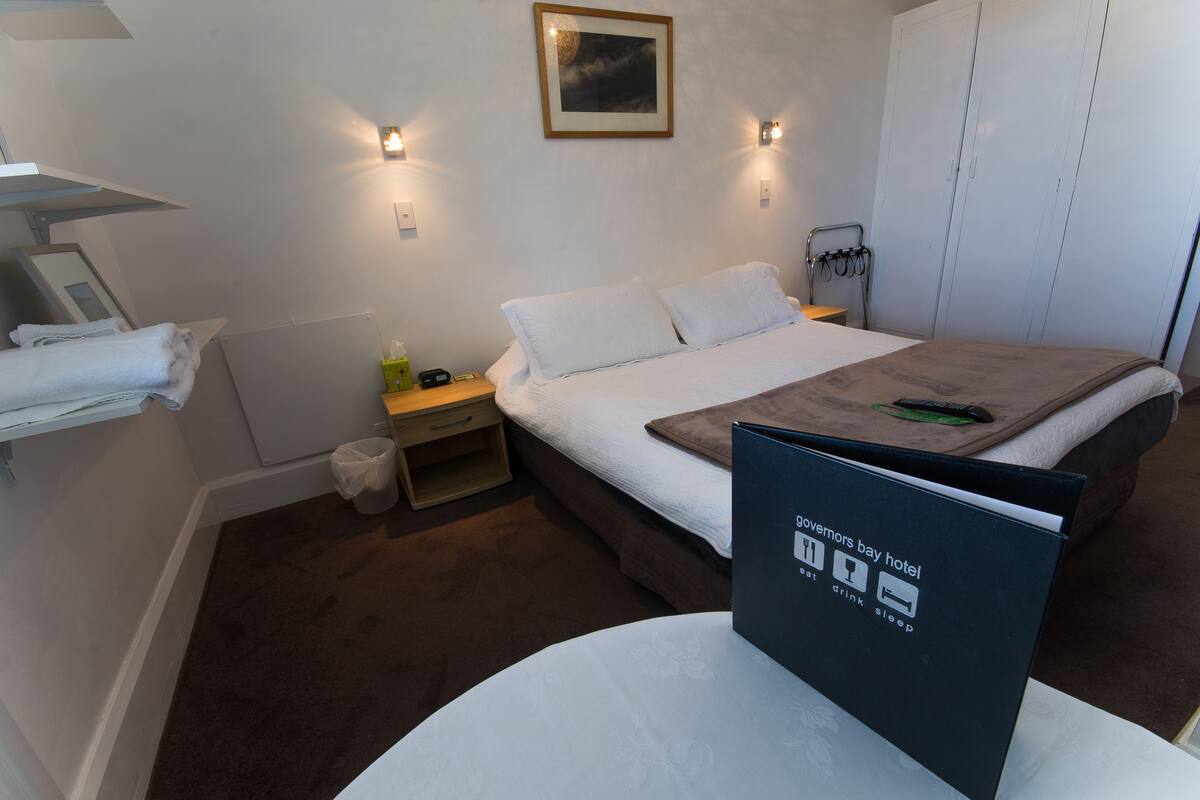 A hotel room with a bed, bedside tables, a small table with a menu, and a framed picture on the wall.