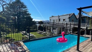 Patio trasero con piscina, cubierta de madera y flotador de flamenco rosa.
