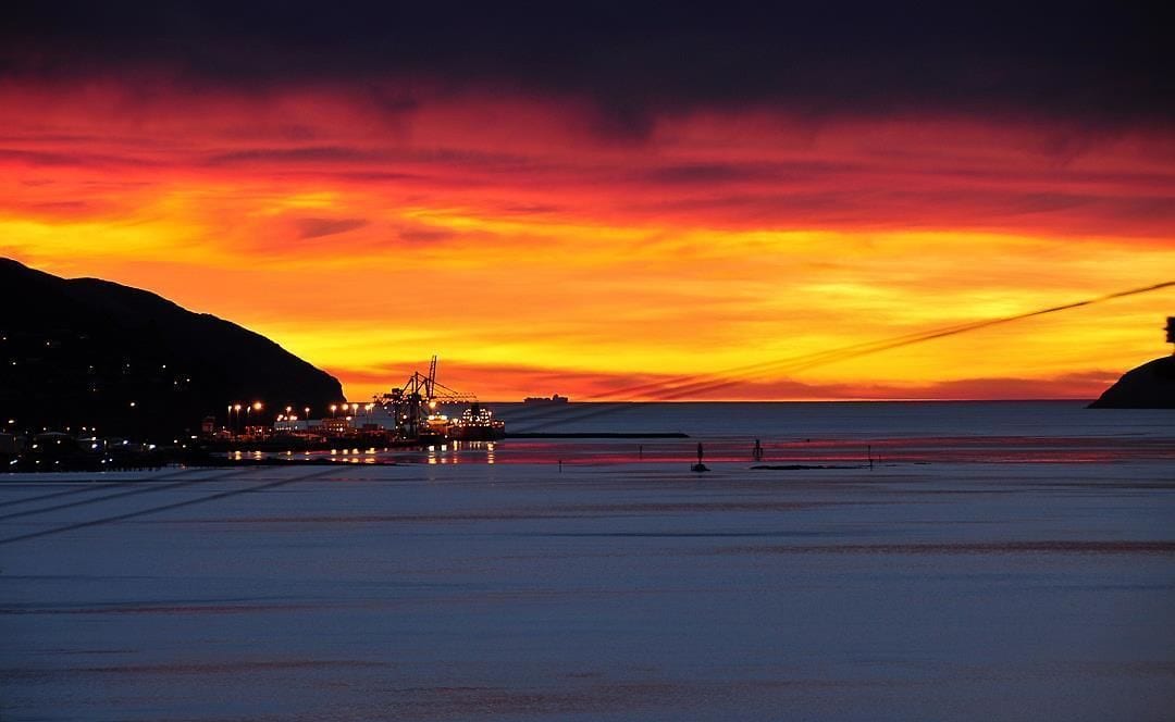 A coastal sunset with a pier extending into the water, buildings on the left, and a clear sky.